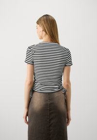 Stripet svart og hvit kortermet topp med rynkete bakdetalj og knytedetaljer, kombinert med et høytlivs brunt denim-skjørt.