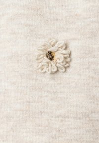 Tissu beige tricoté avec une décoration florale texturée, présentant un détail central doré et des fils doux et bouclés.