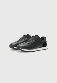 Zwarte sportieve sneakers van leer en gaas, met een gestructureerd oppervlak, een witte zool, een ronde neus en platte veters.