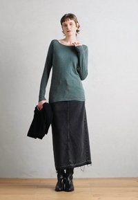 Žalias ilgos rankovės viršus iš minkštos medžiagos, derinamas su juodu džinsiniu maksi sijonu, turinčiu nusiskeltus kraštus ir juodais auliniais batais.