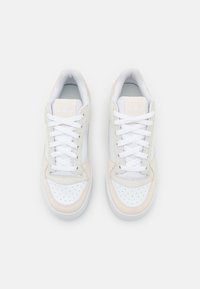 White and beige sneakers with a smooth leather upper, perforated toe, white laces, padded collar, and iconic logo on the tongue.