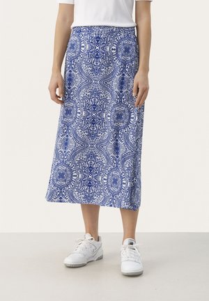 Jupe midi à motifs bleus et blancs portée avec des baskets blanches et un haut blanc à manches courtes, montrée de la taille aux pieds.