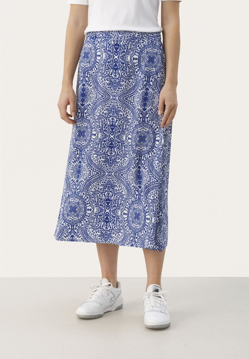 Jupe midi à motifs bleus et blancs portée avec des baskets blanches et un haut blanc à manches courtes, montrée de la taille aux pieds.