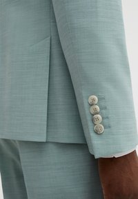 Light blue tailored blazer with a smooth texture, featuring a single vent, four button closure on sleeves, and neat stitching details.