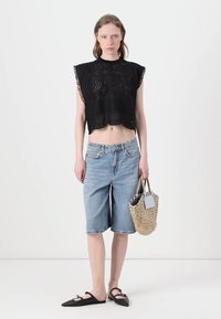 Top nero corto in pizzo con orlo scallopato; pantaloni Bermuda in denim blu chiaro; scarpe nere senza tacco; borsa intrecciata con manico corto.