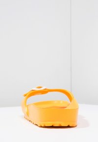 Gul gummisandal med tekstureret sål og en hvid rem. Designet har en åben bagdel og en afrundet form.