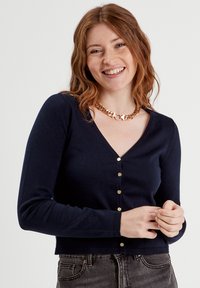Cardigan de punto azul marino con escote en V, mangas largas y botones dorados en la parte delantera. La tela parece suave con puños acanalados.