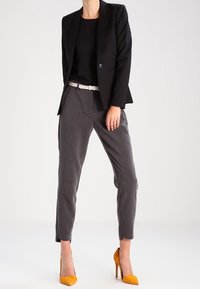Czarna marynarka na czarnym topie, szare spodnie o teksturowanym wykończeniu oraz żółte czółenka na szpilce. Całość uzupełnia biała pasek.