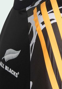 Čierny športový dres s žltými a sivými grafickými vzormi, s priedušnou textúrou látky a výrazným logom značky.