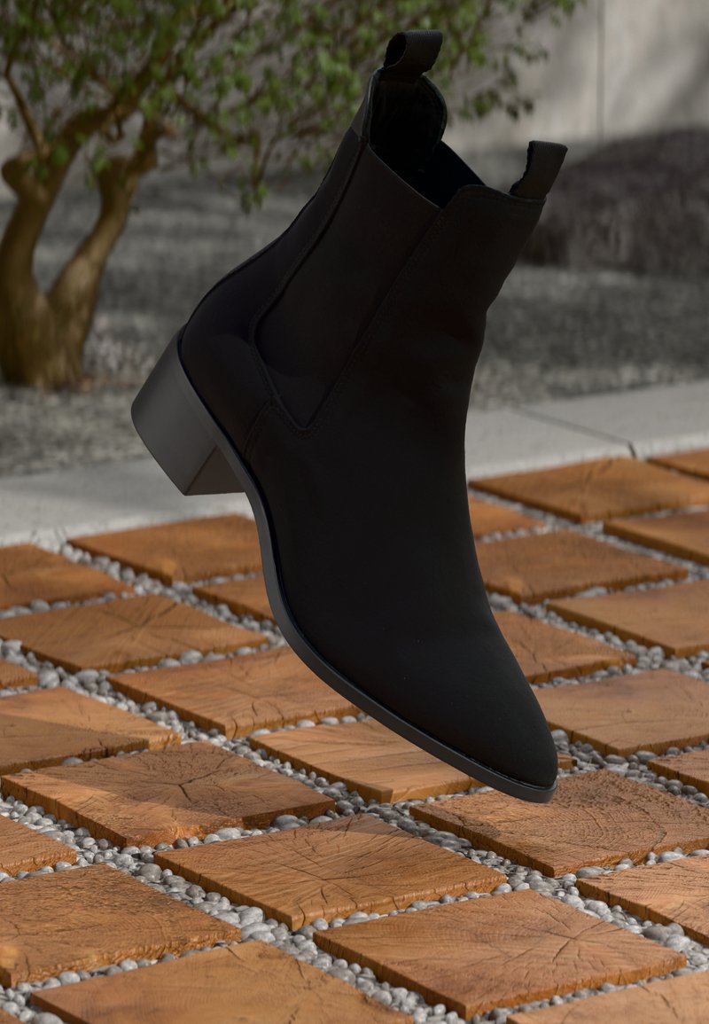 Bottines noires à bout pointu et à petit talon carré. Fabriquées en matériau lisse, elles possèdent des panneaux élastiques latéraux et une languette de tirage.