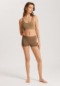 Bralette de tela elástica marrón y conjunto de shorts a juego. El sujetador tiene tirantes anchos y un diseño sin costuras; los shorts son de cintura alta con un acabado suave.