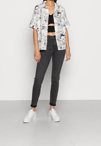 Camisa blanca de manga corta con personajes de dibujos animados en negro, top corto negro con recortes, jeans ajustados oscuros y zapatillas blancas.