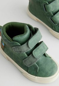 Grüne Leder-Hohe-Topschuhe mit doppeltem Klettverschluss, strukturiertem Oberflächen und einer kontrastierenden weißen Gummisohle.