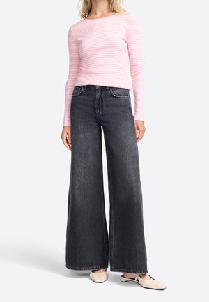 Roze geribd shirt met lange mouwen gecombineerd met high-waisted, wijd uitlopende donkergrijze spijkerbroek en lichtbeige instapschoenen.