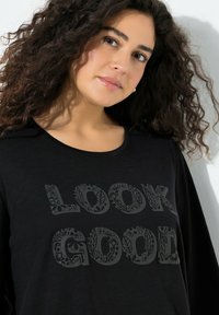 Czarna koszulka z długim rękawem z napisem „LOOK GOOD” w misternych kwiatowych wzorach. Miękki, teksturowany materiał z okrągłym dekoltem.