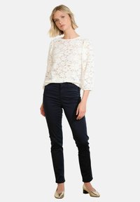 White lace long-sleeve top with a round neckline, paired with dark navy fitted pants and golden block-heel shoes.