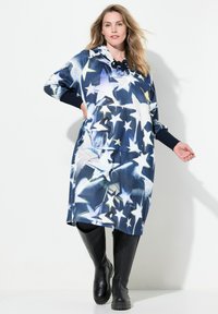 Marinblå oversized hoodieklänning med stjärnmönster, som har långa ärmar, sidfickor och en justerbar huva. Knälång design, mjuk textur.