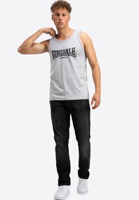 Hallhalli hall tooni puuvillane T-särk, millel on väljapaistvalt must logo "LONSDALE LONDON", kujundatud klassikalises serif-kirjas. Kandnud tumedate teksade ja valgete sneakersitega.