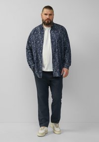 Marineblauw gestreepte overhemd met knopen over een wit T-shirt, gecombineerd met donkere broeken en lichtgekleurde schoenen. Casual pasvorm, ontspannen ontwerp.