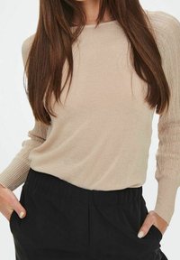 Beige gebreide trui met lange mouwen en geribbelde textuur; gecombineerd met zwarte, hooggetailleerde broek. Gladde stof, comfortabele pasvorm.