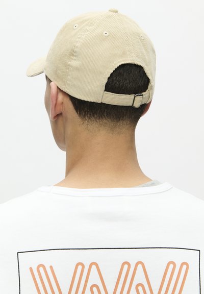 Beige kordbársony sapka ívelt silddel, állítható pánttal hátul és látható varrásokkal. Fehér inggel viselve, narancssárga grafikával.