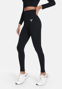 Čierne legíny s vysokým pásom a rebrovaným opaskom, s bielym logom. Vyrobené z elastického materiálu, majú hladkú, priliehavú textúru.