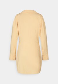 Camisa de mangas compridas em amarelo claro, com colarinho e punhos abotoados, com uma textura suave e leve e um corte ajustado.