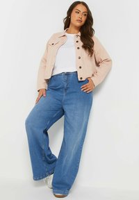 Vaaleanpunainen lyhyt takki mustilla napeilla, yhdistettynä väljiin sinisiin farkkuihin. Asu sisältää yksinkertaisen valkoisen topin alla.