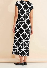 Svart och vit klänning med kapärmar och geometriskt mönster, knälång design, slät textur och platta svarta skor.
