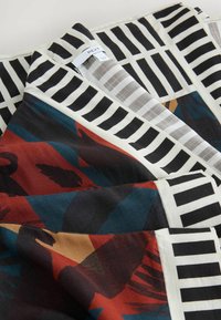 Printed scarf featuring floral patterns in red, blue, and brown on a black background; contrasted with striped edges in black and white.