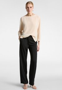 Blusa fluida color crema con maniche lunghe, abbinata a pantaloni neri su misura. I dettagli notevoli includono un colletto rotondo e una leggera drappeggiatura.
