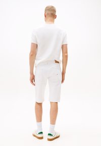 Hvit bomulls t-skjorte kombinert med hvite denimshorts, med baklommer. Fottøyet inkluderer hvite joggesko med grønne detaljer og hvite sokker.