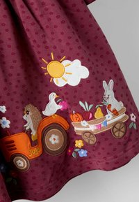 Bordeaux jurk met kleine bloemenprint, voorzien van kleurrijke borduurwerk van een tractor, konijn, egel en kar met fruit, zon en wolken.
