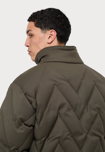 Olíva zöld steppelt dzseki magas gallérral, geometrikus csevegő mintával és texturált, párnázott felülettel.