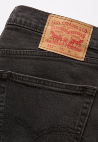 Svarta denimjeans med slim fit, med en tan läderetikett med röd tryck på midjan, samt klassiska sömnadsdetaljer på fickorna.