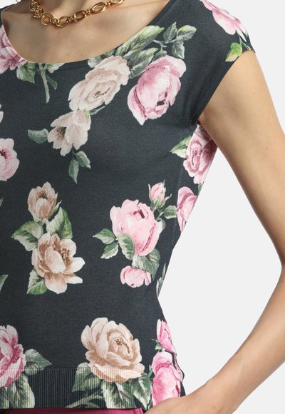 Femme portant un haut noir ajusté avec un imprimé floral de roses roses et beiges et un collier chaîne épaisse en or.