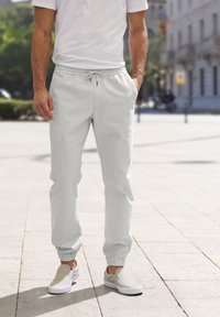 Lichtgrijze joggers met een elastische tailleband en boorden, voorzien van een trekkoord. Gecombineerd met beige instappers. Glad weefsel.
