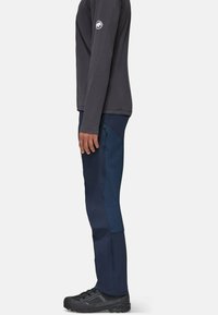 Pantalones de exterior en navy con paneles laterales texturizados, forma ajustada, bolsillo con cremallera, combinados con zapatos de senderismo negros y una camiseta de manga larga oscura.