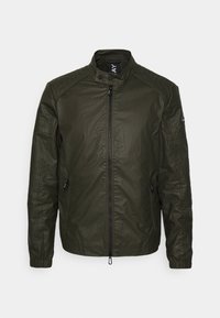 Olivgrön jacka i texturerad tyg, med hög krage, dragkedja fram och två sidofickor med dragkedjor. Avslappnad stil.