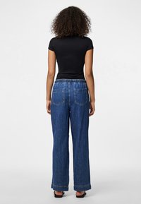 Camisa preta de manga curta com um design ajustado, combinada com jeans de ganga azuis de perna larga com um cós elástico e bolsos traseiros.