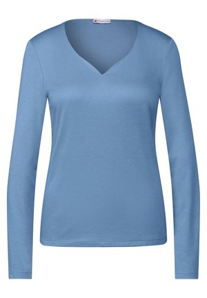 Chemise femme bleu clair à manches longues avec un col en V et une taille cintrée, affichée sur un fond blanc uni.