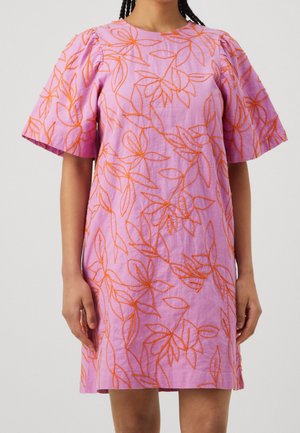 Robe rose à manches courtes avec broderie florale orange, encolure ronde et manches légèrement bouffantes, portée par une personne debout.