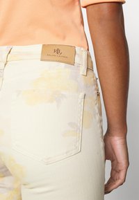 Květinové kalhoty světle žluté barvy s hladkou texturou, na pásku s embosovanou koženou nášivkou "Ralph Lauren" v barvě tan.