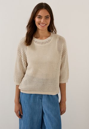 Light beige, loose-knit sweater with a crew neckline and three-quarter sleeves. Paired with loose blue denim pants.