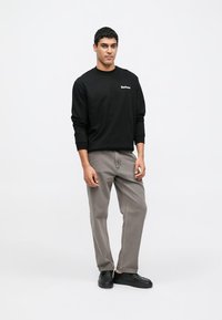 Černá mikina s dlouhým rukávem s logem "Barbour", doplněná o šedé kalhoty s volným střihem a černé nazouvací boty. Jednoduchý design, hladká látka.