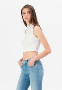 Weißes geripptes Croptop mit hohem Kragen, kombiniert mit hellblauen Skinny Jeans mit vorderen Taschen und leichtem Verblassen.