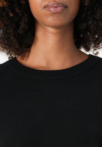 Maglione nero a maglia con colletto rotondo a coste e texture liscia, che mette in risalto una vestibilità aderente attorno alle spalle e all'area del collo.