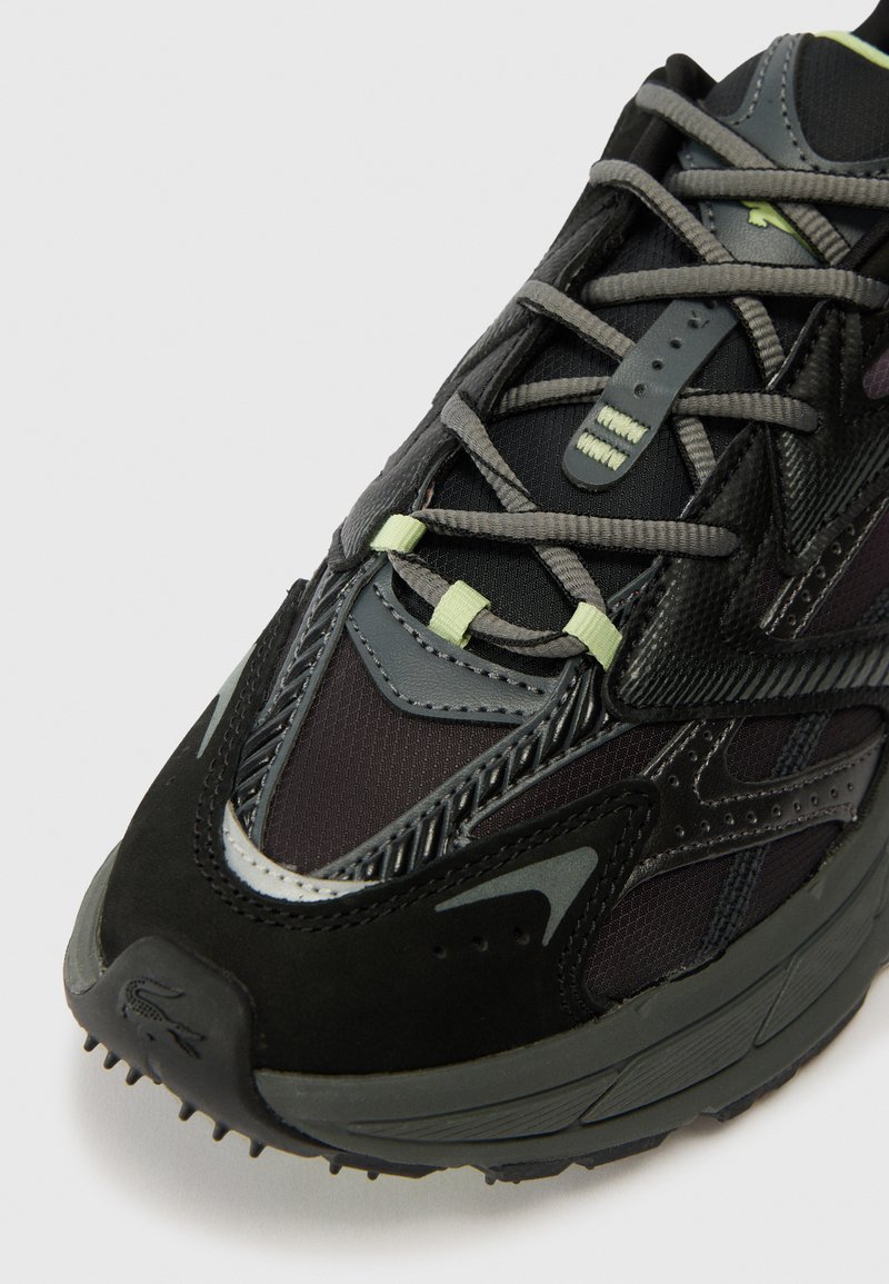 Close-up of black and dark gray athletic shoe with light green lace loops and textured synthetic upper.