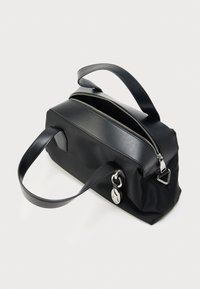 Czarna prostokątna torebka z dwoma skórzanymi uchwytami, częściowo otwartym srebrnym zamkiem błyskawicznym oraz srebrnym okrągłym breloczkiem po boku na białym tle.