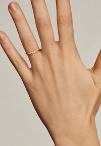 Anillo de oro con pequeñas piedras preciosas engastadas en una línea, llevado en una mano extendida, con un acabado pulido y un diseño de banda delgada.